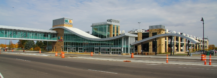 Modern glass-front transit station with curved white rooflines and covered pedestrian walkways.