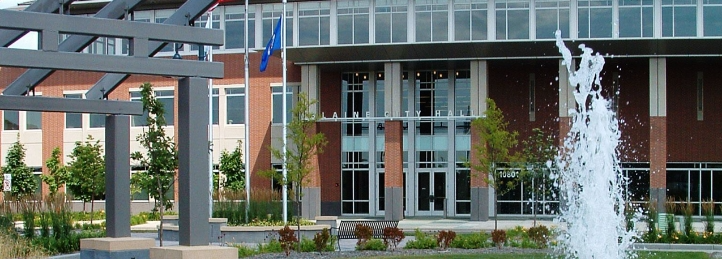 Modern civic building entrance with landscaped plaza, fountain, and glass facade.