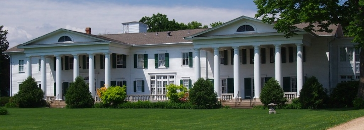 Large white colonial-style mansion with tall columns, manicured lawn, and symmetrical architecture.