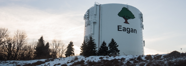 Eagan water tower with city name and tree logo overlooking a snowy hillside at sunset.
