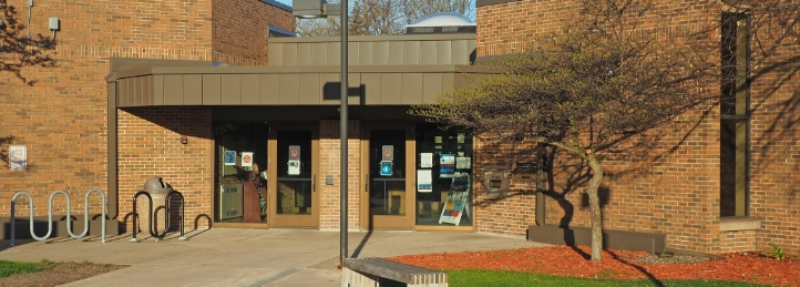 Brick civic or community building entrance with glass doors, landscaped walkway, and modern exterior lighting.