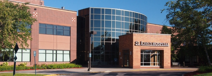 Entrance to St. John's Hospital with curved glass facade, brick exterior, and landscaped grounds.