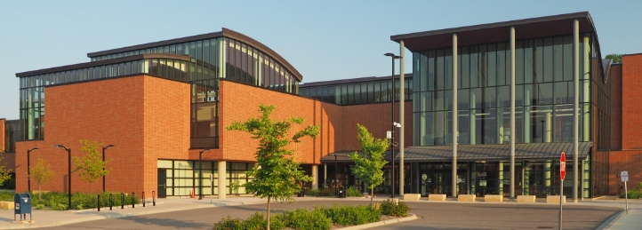 Modern civic or educational building with large glass windows, brick exterior, and landscaped entrance plaza.