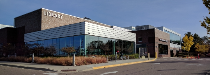 Modern public library building with large glass windows, landscaped entrance, and contemporary architecture.