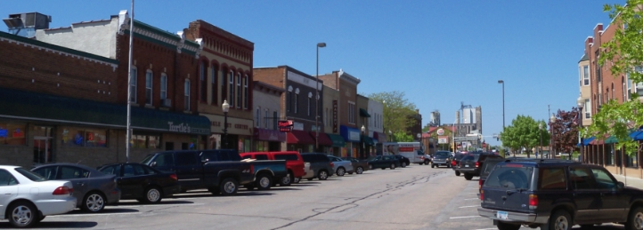 Historic downtown main street with brick storefronts, parked cars, and local businesses on a sunny day.