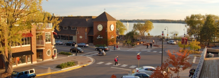 Lakeside downtown intersection with clock tower, waterfront views, and autumn trees at sunset.